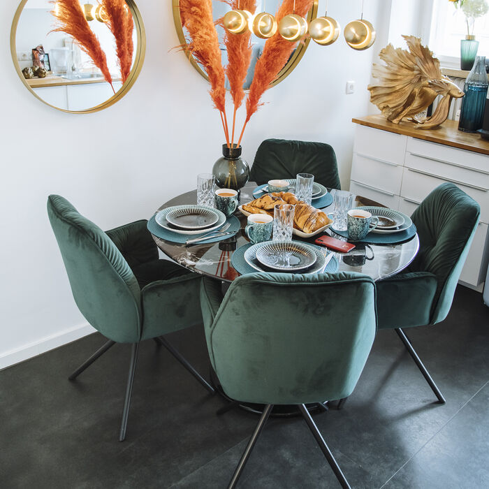 Magnifique chaise look velours de couleur vert avec accoudoir Mila de la marque Kare Design exposé dans une salle à manger autour d'une table ronde décorée